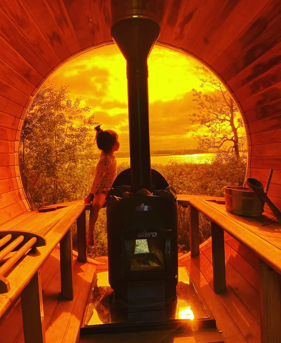 A small child enjoying the outdoor dry sauna looking outside during a sunsset