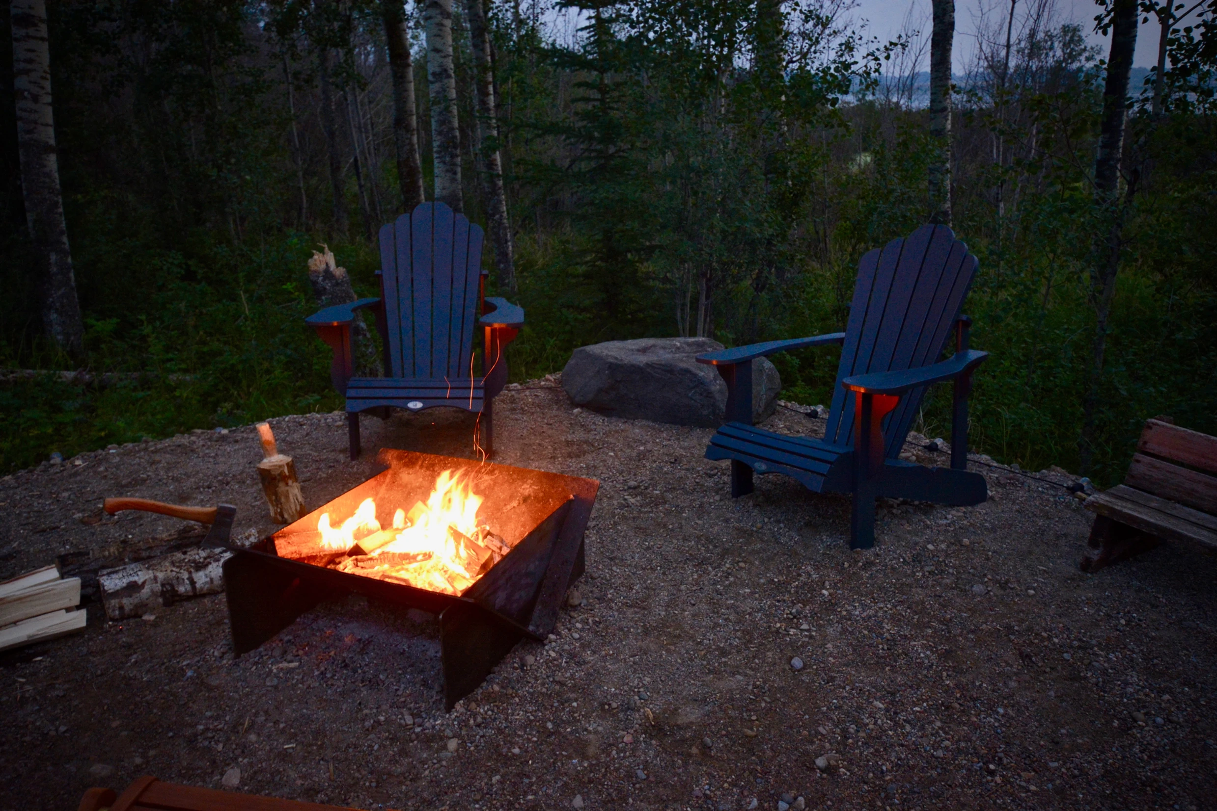 Large fire pit outside of ignis dome with two patio chairs with large roaring firing during the evening. 
