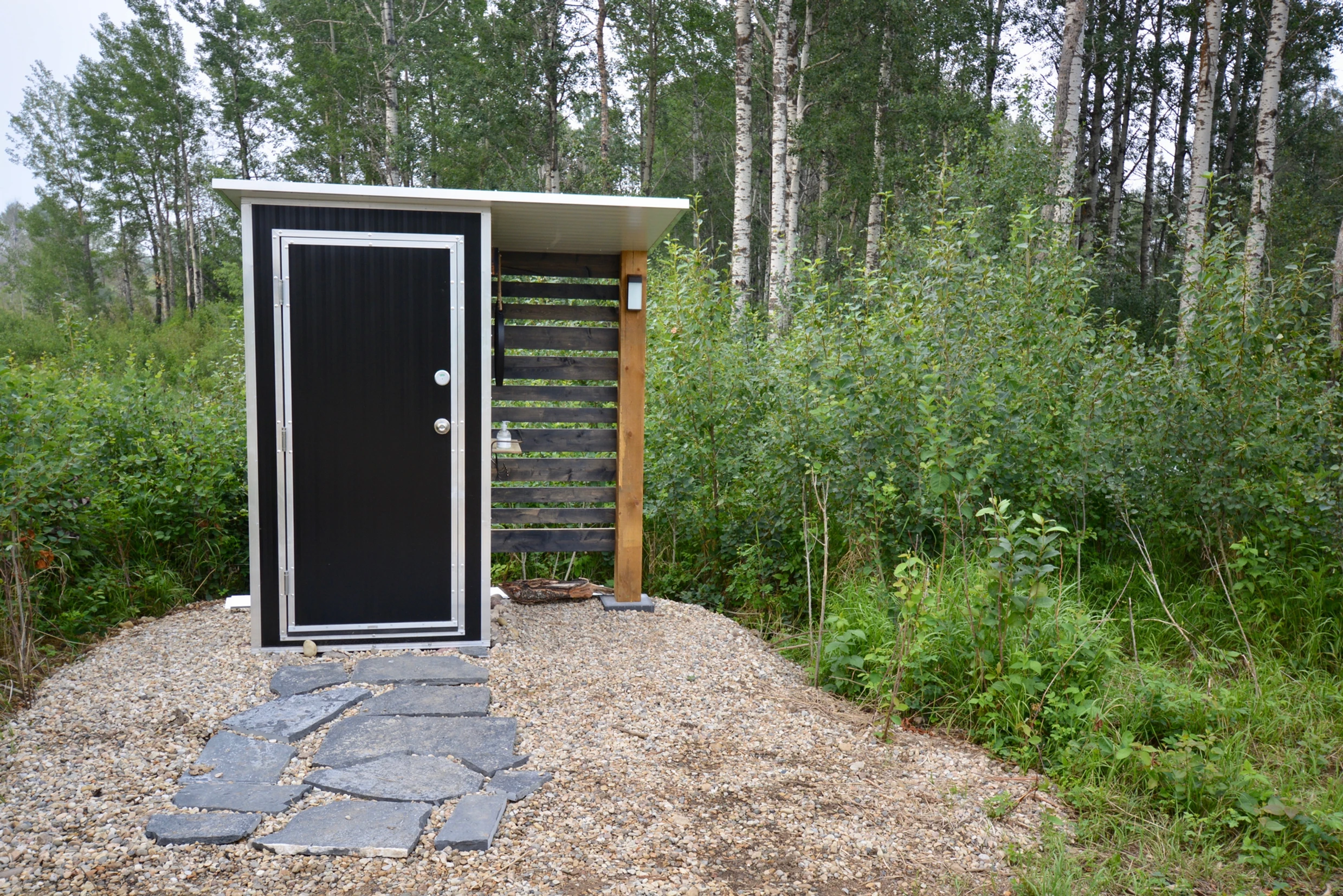 entrance to outdoor shower for ignis dome with forest in the background and paving stones leading up to the door