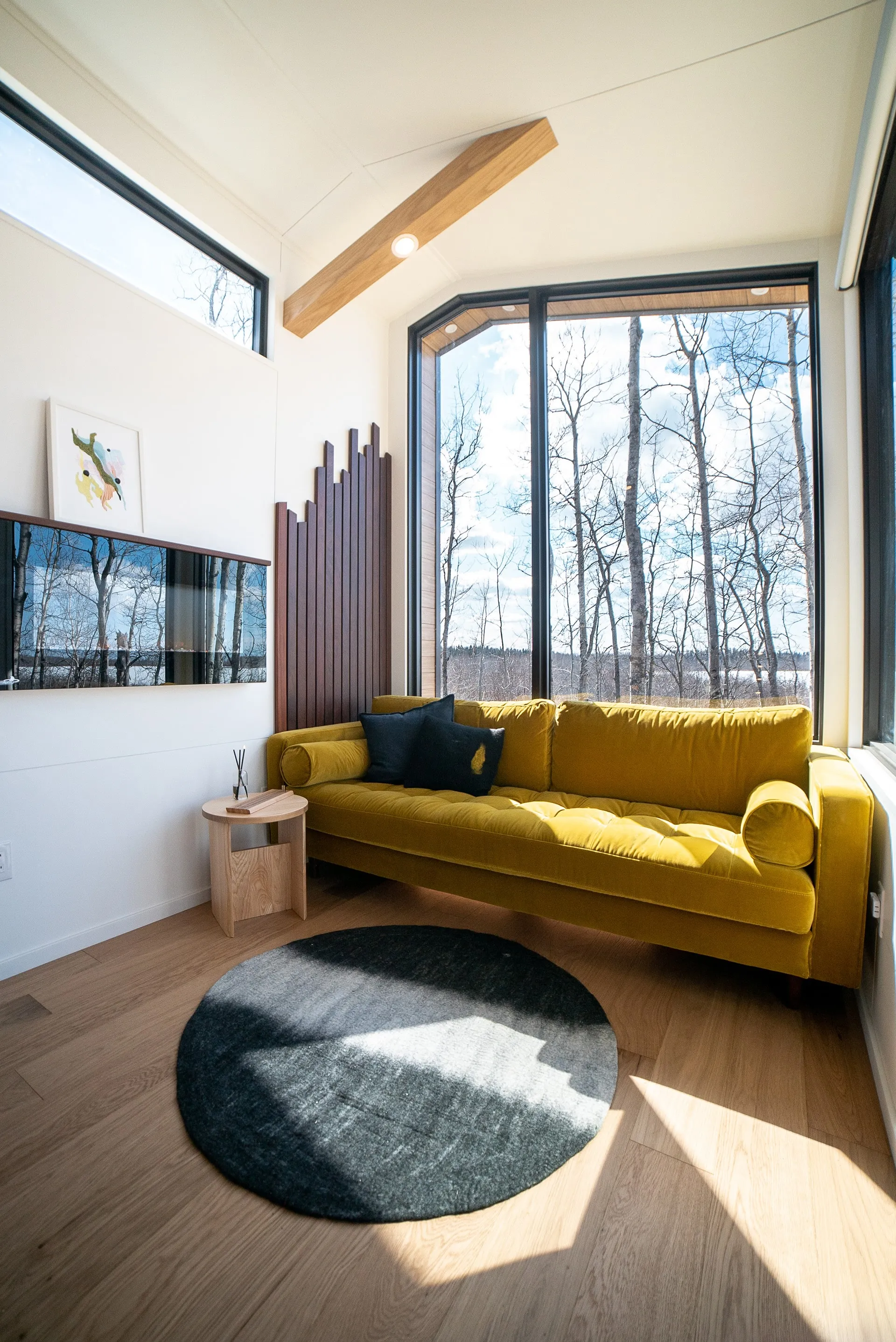 Angled view of Aqua tiny homes living room space with yellow double couch, floating fireplace, feature slat wall and large angled windows